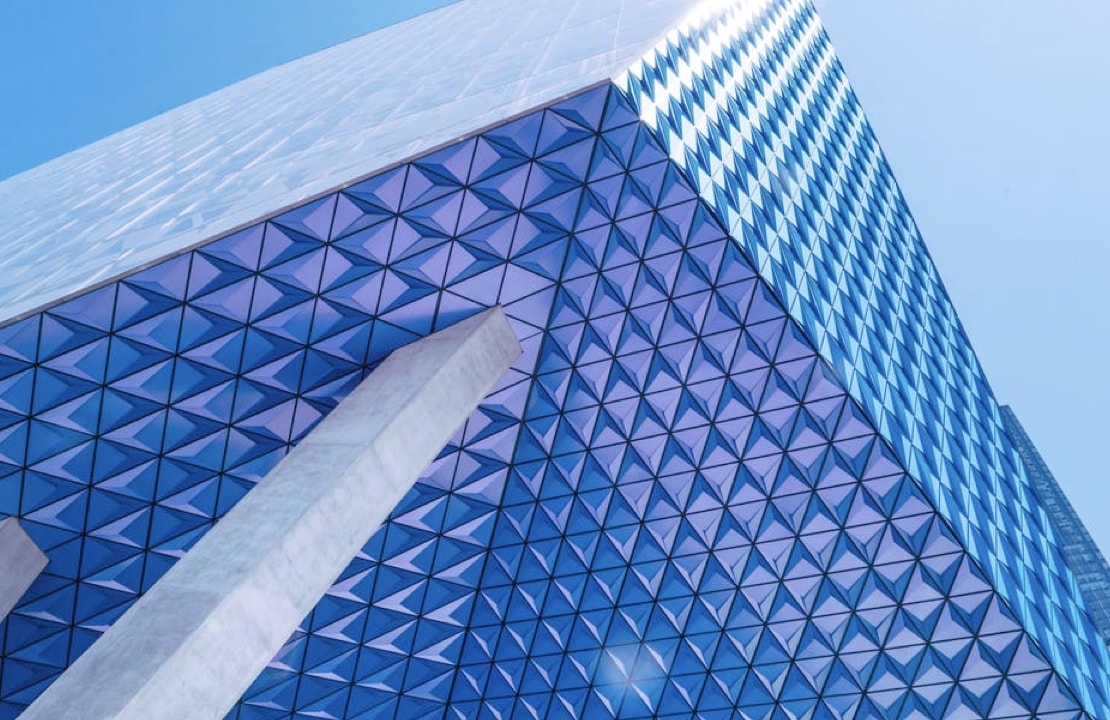 A creative corner shot from below a bright blue structure with a three-dimensional pattern adorning the walls. A concrete supporting pillar can be seen.